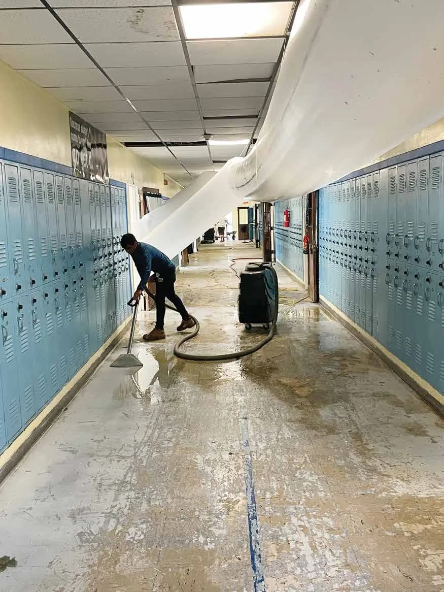 A technician extracting standing water from a school hallway